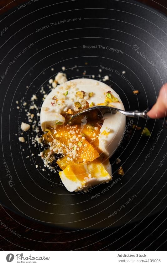 Anonymous woman eating stylish dessert with spoon restaurant confectionery jelly glazed arm hand using bowl plate nut sweet healthy organic panna cotta portion