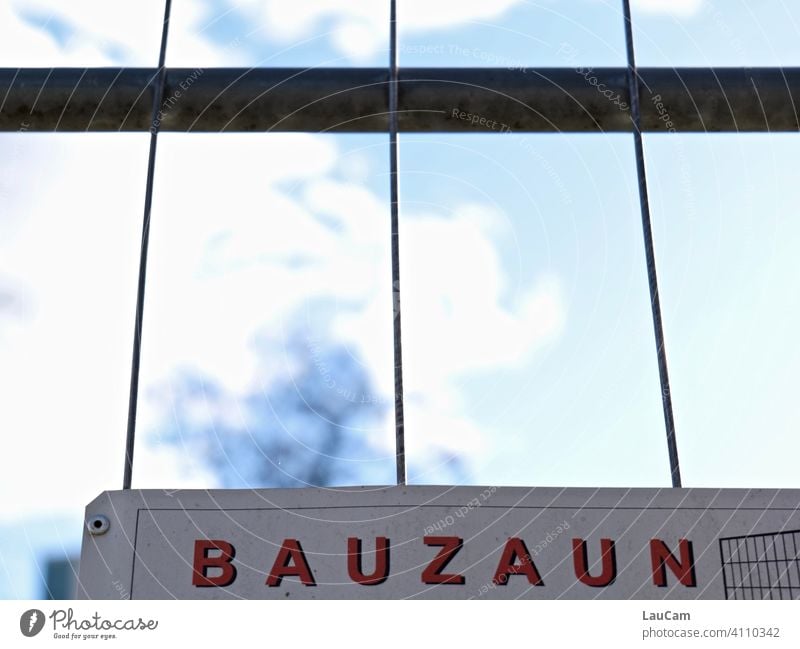 Construction fence sign on construction fence in front of sky blue with clouds and tree Hoarding Fence Gap in the fence Construction site Signs and labeling