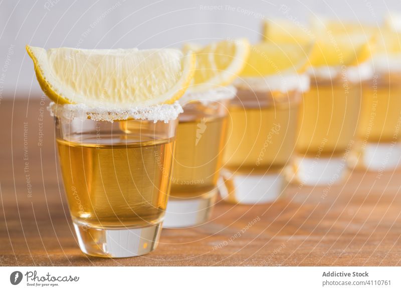 Shots of alcohol with slices of lemon on top shot tequila piece booze row glass table wooden wall drink beverage refreshment tasty cold orange citrus bar juice