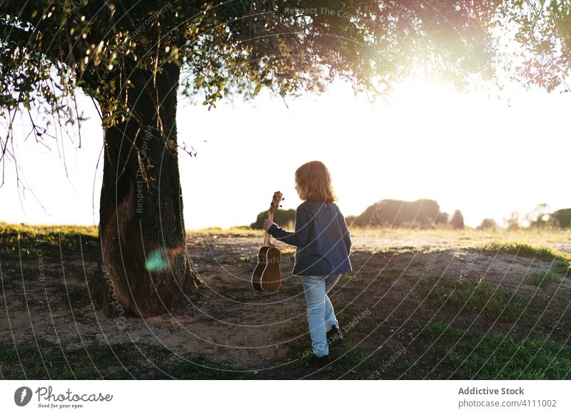 Little girl walking under tree and playing ukulele kid music guitar nature child summer little instrument sound song melody trunk perform practice talent learn