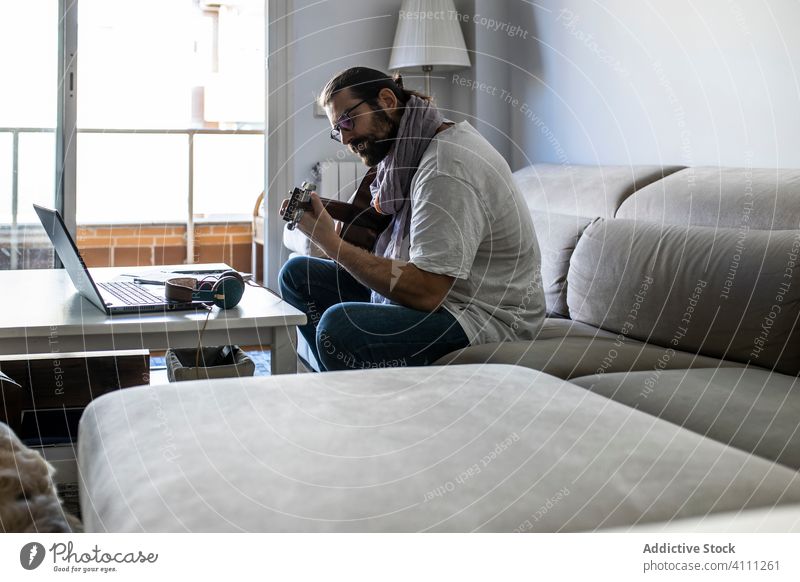 Stylish guitarist on couch in living room man play sit sofa male casual music songwriter composer poet home lifestyle talent instrument melody perform lesson