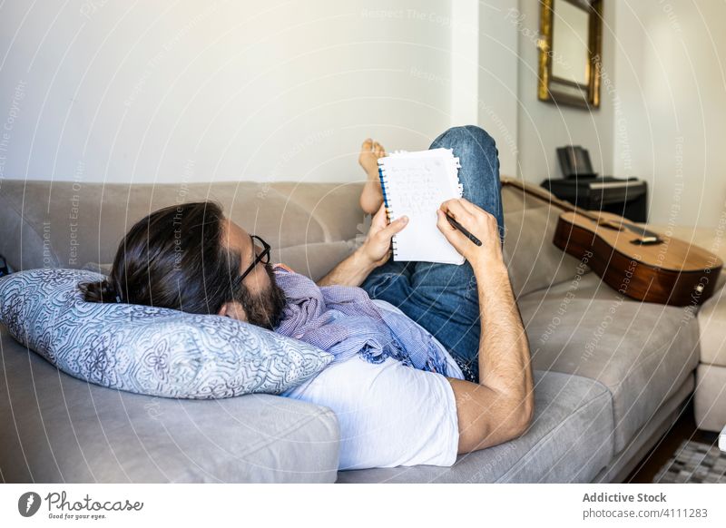 Man writing notes on couch in cozy living room man write sofa male casual comfort songwriter lying poet composer relax home apartment young pillow rest read