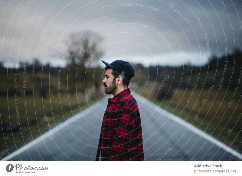 Traveler on road in countryside man walk nature adventure travel trip field empty route cloudy overcast sky asphalt rural path way journey activity destination