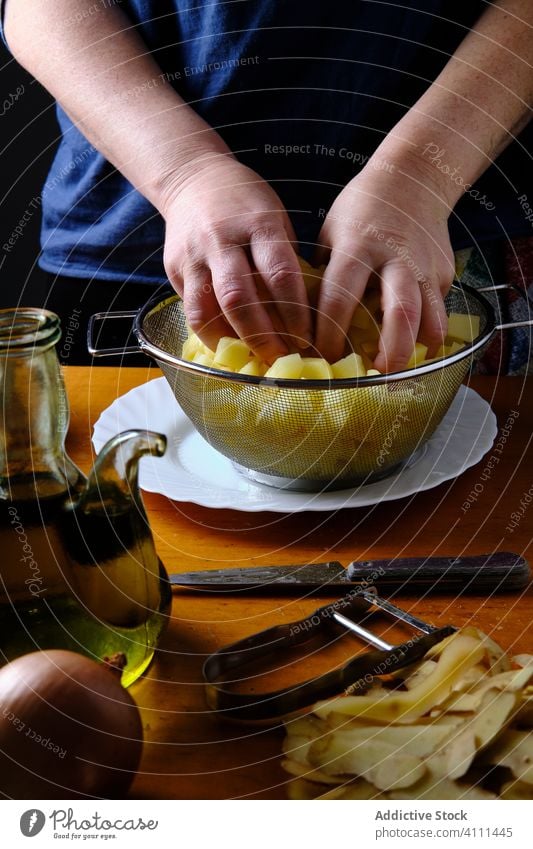 Anonymous woman preparing pieces of potatoes for dish with sieve chef cook prepare process slice fresh food kitchen homemade ingredient organic raw recipe table