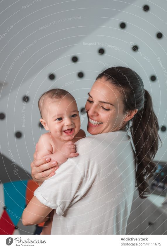 Joyful mother with baby in bedroom carry smile laugh enjoy satisfied little happy kid child adorable love cute together care tender affection hug small home