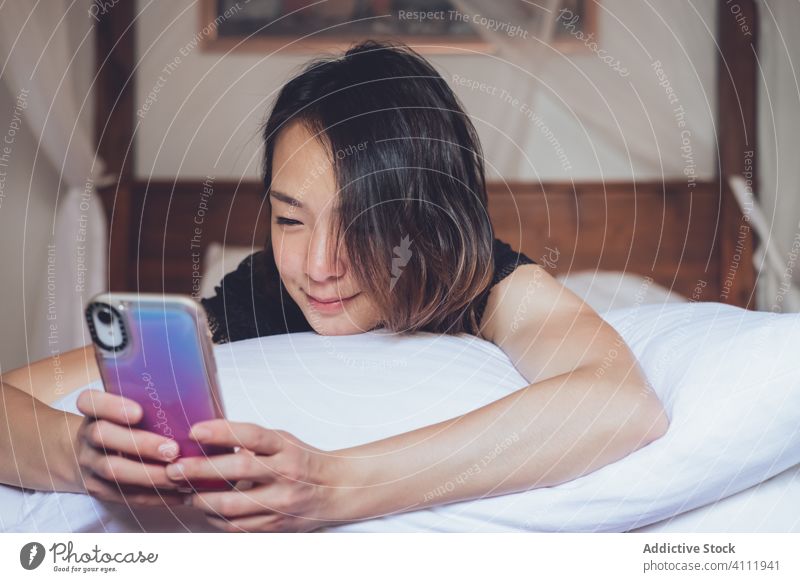 Happy Asian woman using smartphone in bed happy smile ethnic pillow home cozy female relax rest bedroom young comfort device gadget browsing watch lifestyle