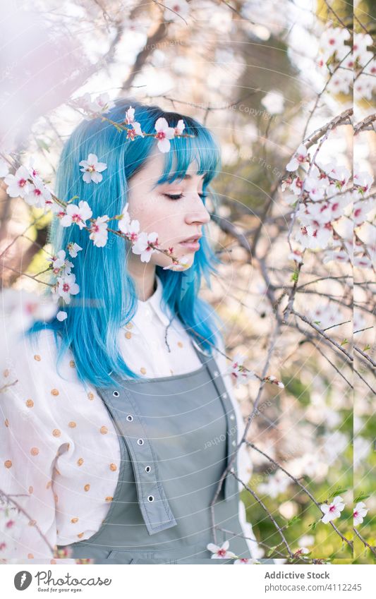 Trendy woman in blooming garden spring teen smell fragrance alternative dyed hair flower style trendy modern young blue hair blossom tree female nature floral