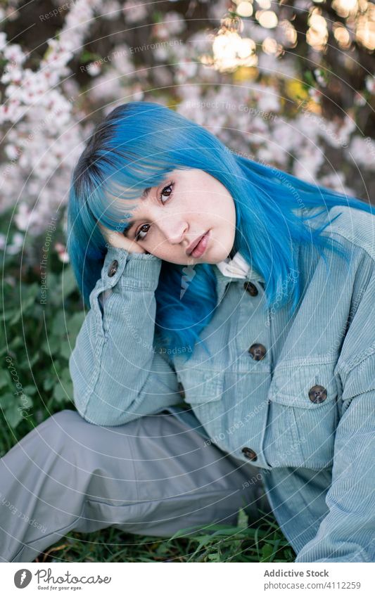 Thoughtful young woman sitting in blooming garden trendy sad teen melancholy dyed hair alternative solitude thoughtful style pensive tree blue hair park flower