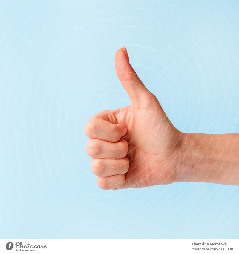 Closeup of female hand showing thumbs up sign against pastel blue background, copy space, minimal concept woman finger symbol business arm good person positive