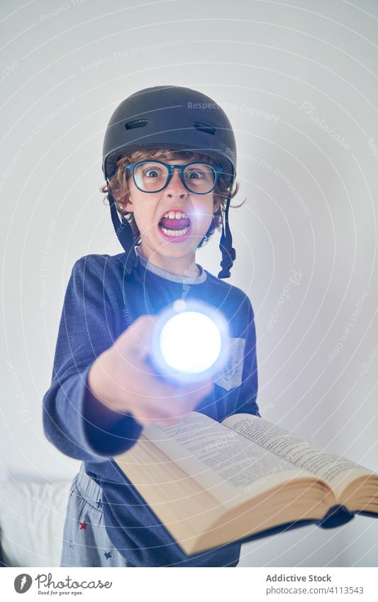 blond kid in pajamas with a helmet a flashlight and a book playing research children game protect happiness enjoyment room indoor party comfort emotional