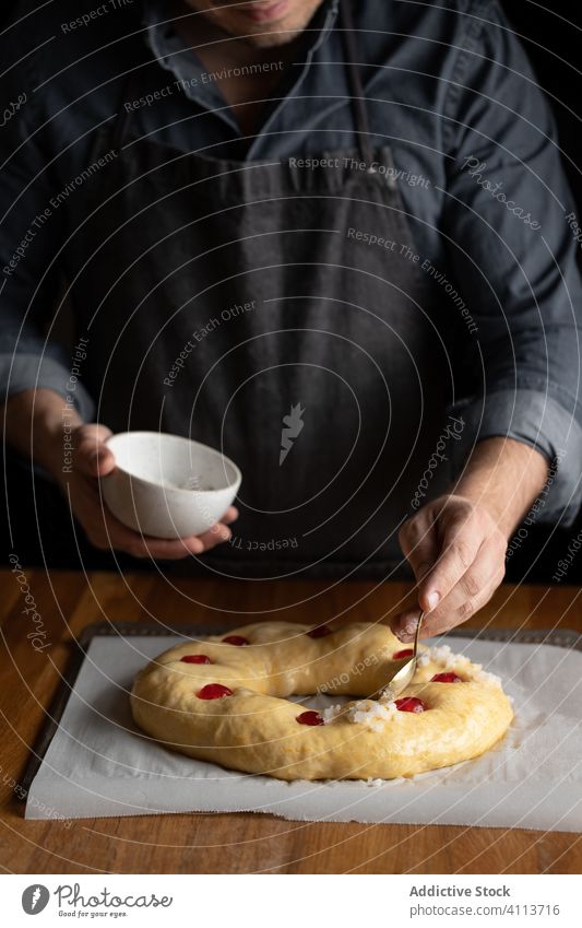 Baker preparing bread at wooden table food prepare cook chef egg yolk dough round uncooked brush man bakery pastry meal culinary homemade kitchen tasty