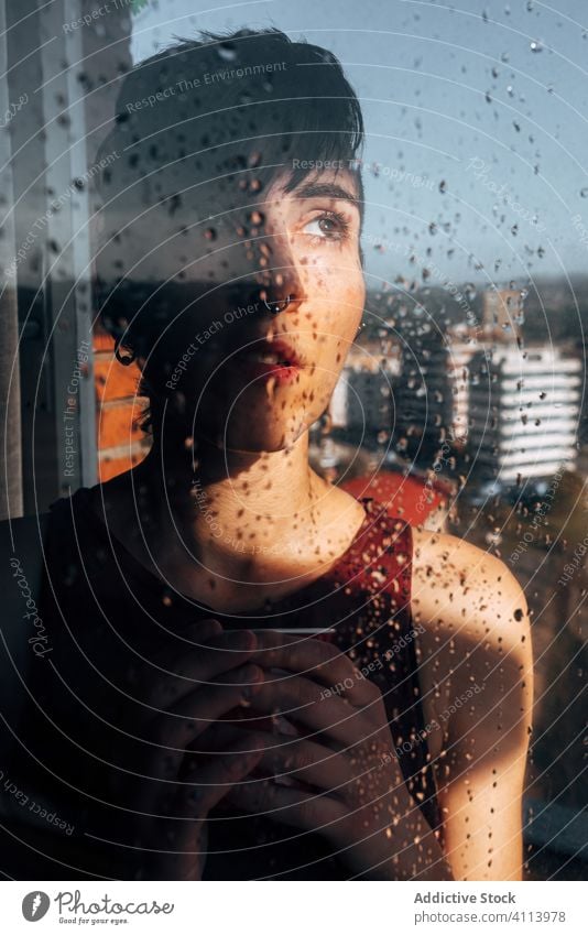 Thoughtful woman drinking coffee near window sad depression self isolation home unhappy lonely covid19 melancholy young female wet rain solitude stress cup