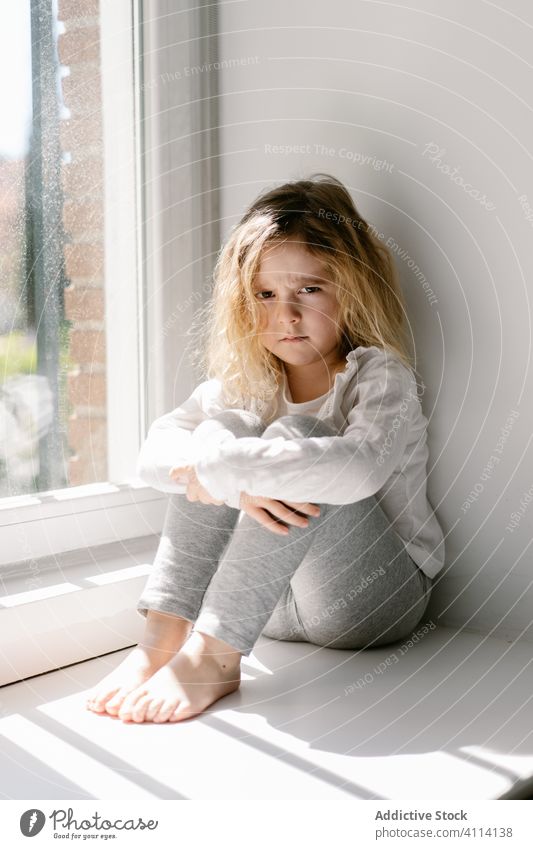 Upset child showing grimace while sitting on window sill barefoot girl upset capricious annoyed kid childish expressive angry sad little unhappy childhood