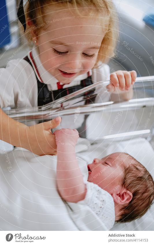 Happy girl standing near newborn sibling baby sister happy sleep hospital crib cradle child kid little care childhood neonatal together childcare cheerful love