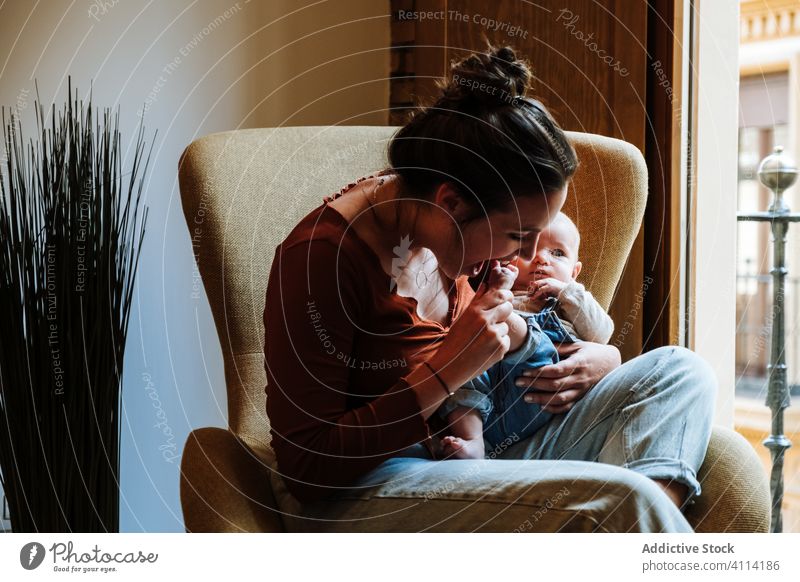 Mother with baby sitting near window mother baby talk chair home cozy comfort casual happy cute love tender woman infant adorable barefoot child kid smile