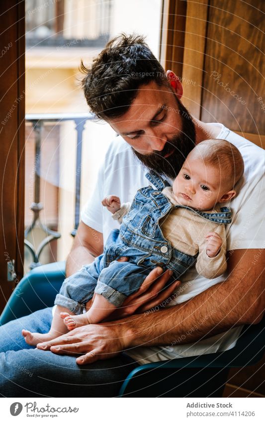 Bearded father with baby sitting near window beard communicate hug home love tender cozy chair man infant kid child little embrace parent cuddle close