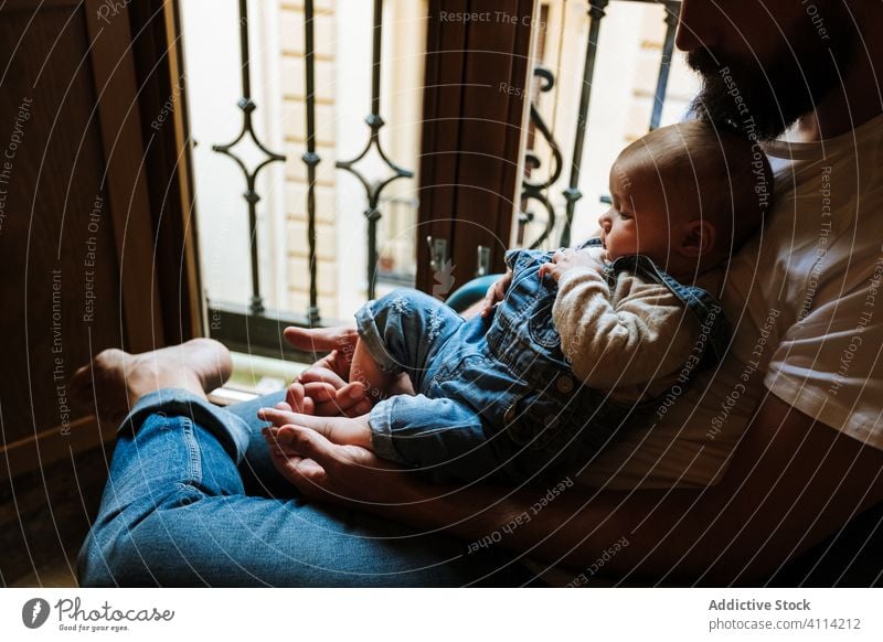 Bearded father with baby sitting near window beard communicate hug home love tender cozy chair man infant kid child little embrace parent cuddle close