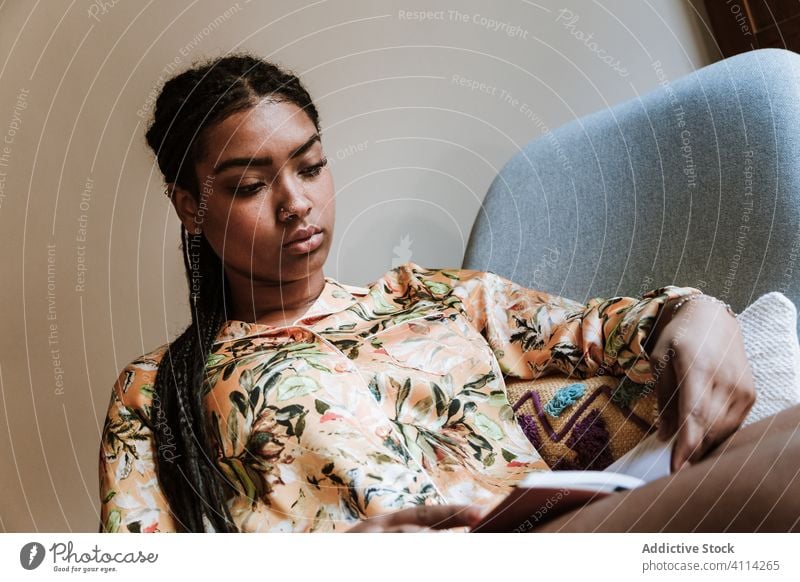 Ethnic woman with book resting at home read african american black casual chair brunette calm sitting young cozy ethnic piercing free time relax lifestyle