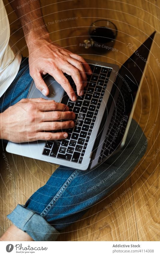 Bearded freelancer using laptop at home man sitting typing drink floor project modern male casual device work internet lifestyle gadget browsing data guy remote