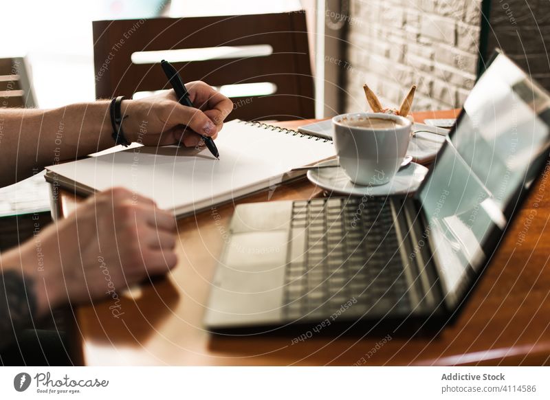 Crop freelancer drawing in notebook in cafe man sketch coffee laptop table remote project male notepad cup student drink cafeteria computer education restaurant