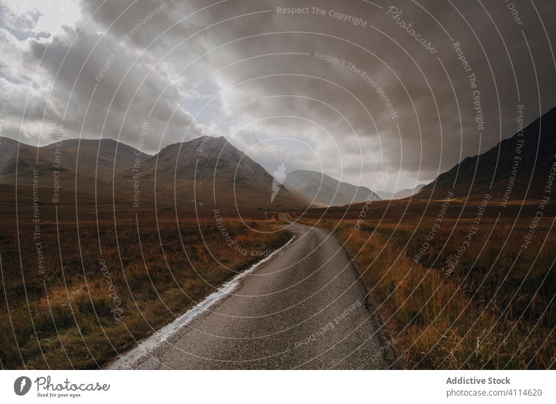 Asphalt road in hilly countryside cloudy sky narrow asphalt grass green nature landscape rural scenic dramatic terrain path way track trail overcast gray nobody