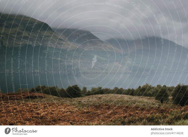 Foggy landscape with mountains and lake fog mist cloud rock highland range calm tranquil water nature cold peaceful scotland gloomy shore travel tourism