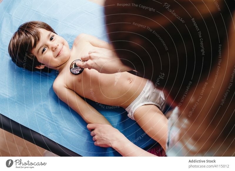 Doctor with stethoscope examining kid in clinic doctor examine cheerful smile hospital little boy lying couch chest respiratory patient health care medicine