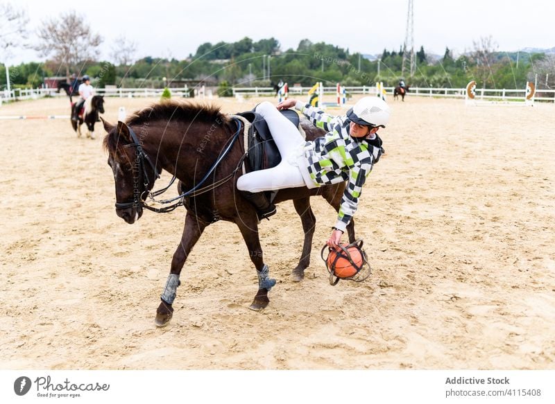 Teen playing game with pink ball from horse teen fall training arena horseback sand lesson school jockey boy ground brown equestrian saddle animal ride friend