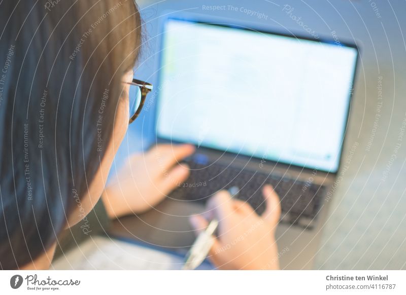 Looking over the shoulder of a young woman with glasses working on a notebook at home. Home office. Online lecture. Homeschooling. home office online lecture