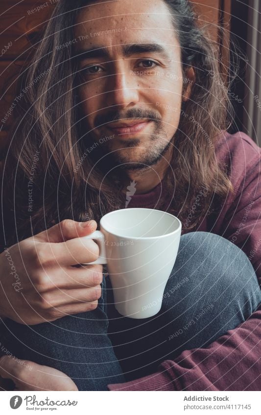 Bearded man resting with hot beverage drink home stay at home coronavirus covid-19 cozy mug mood adult room male relax tea coffee cup comfort long hair beard