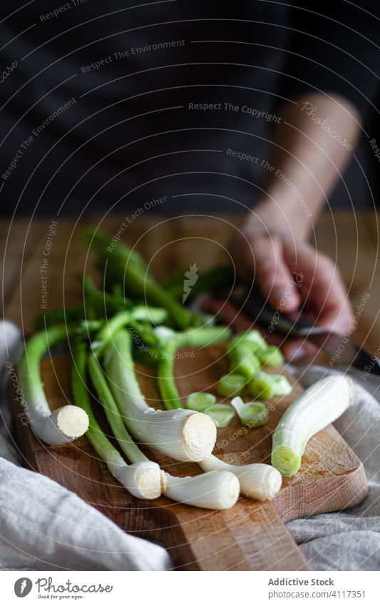 Anonymous person with fresh scallions on cutting board napkin table rustic kitchen ripe cloth composition bunch wooden vegetable food home towel plant cook