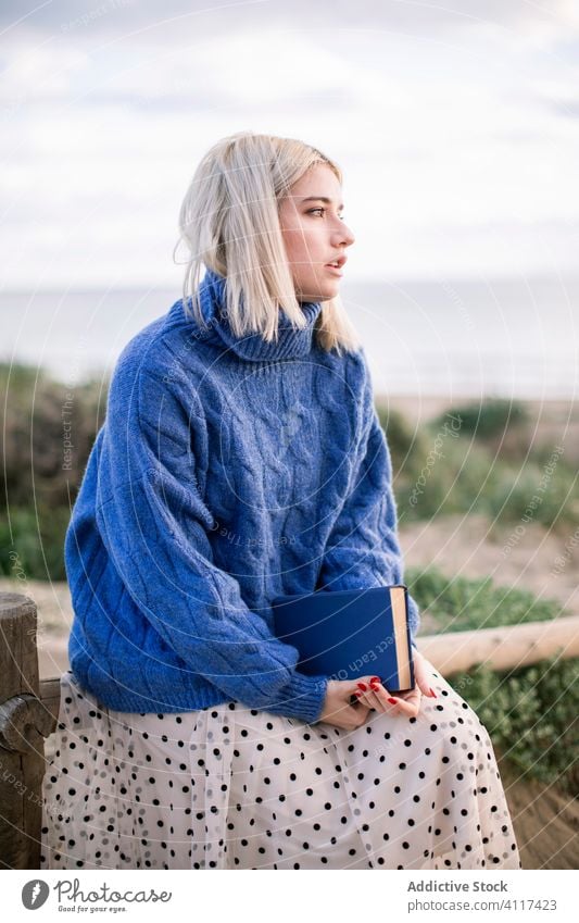 Pensive woman enjoying book in countryside read nature sweater young female casual blonde rest literature hobby happy charming style blue warm holiday travel