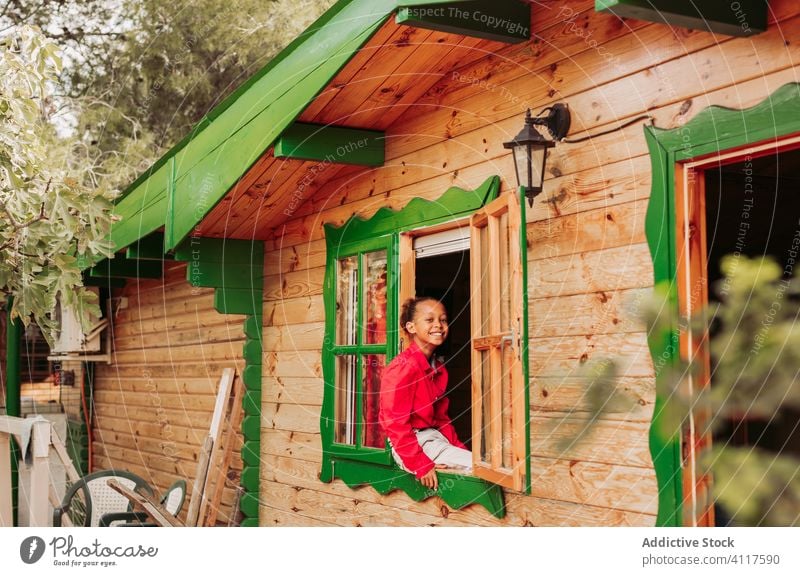 Happy ethnic kid looking out window house happy cheerful wooden rural smile home child lifestyle countryside joy little casual childhood black african american