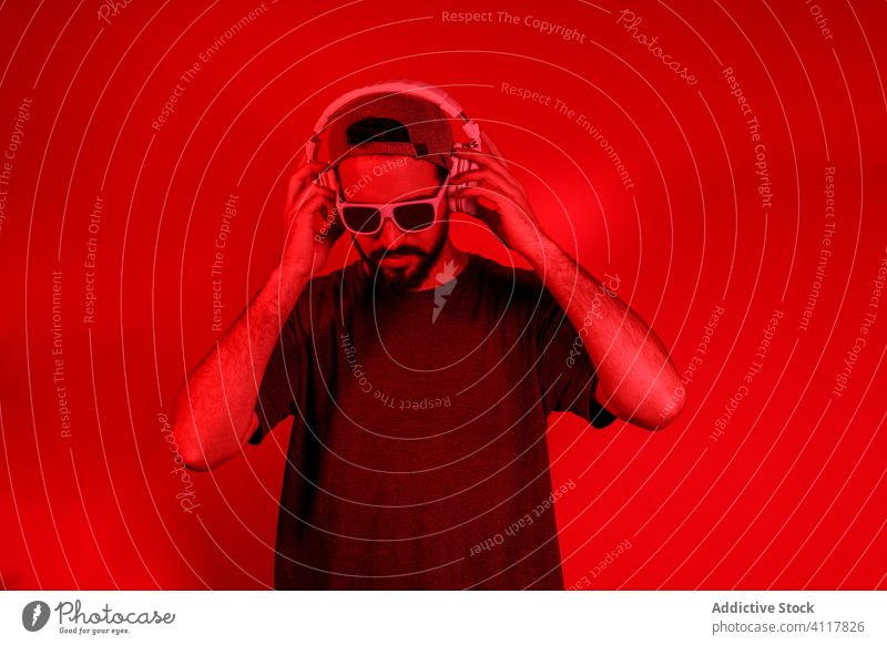 Bearded man listening to music in headphones style modern beard red light bright nightlife male illuminate neon device vibrant gadget sound casual hat entertain