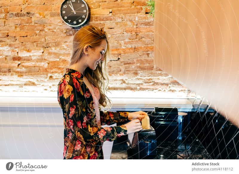 Young woman preparing toasts in morning breakfast prepare kitchen toaster home cozy female young lifestyle relax trendy blonde bread meal dish blouse shirt