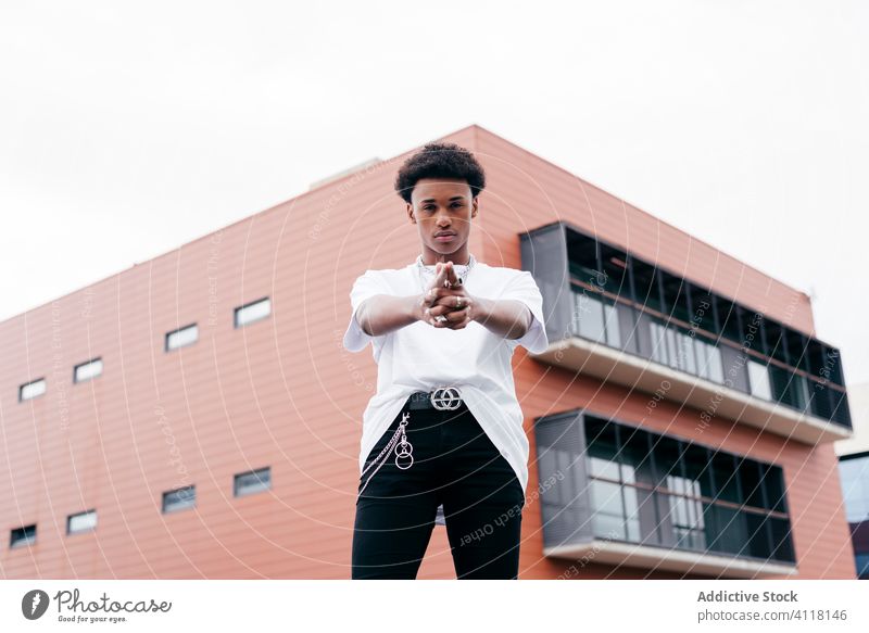 Trendy black guy standing against city building man style trendy street urban accessory gangster cool gun gesture sign modern fashion ethnic confident young