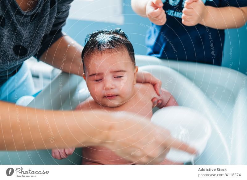 Mother with little son washing baby in bathtub woman mother children dibling care newborn bathroom ethnic bowl love gentle together cute help warm parent foam