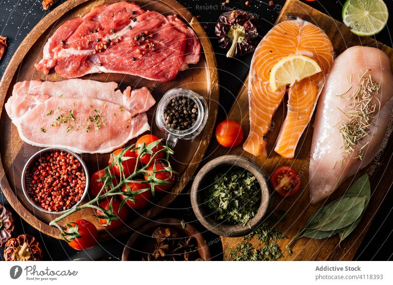 Flat lay of proteins surrounded by spices and seasonings on table product meat salmon condiment fish fillet food pepper cutting board spoon aromatic assorted