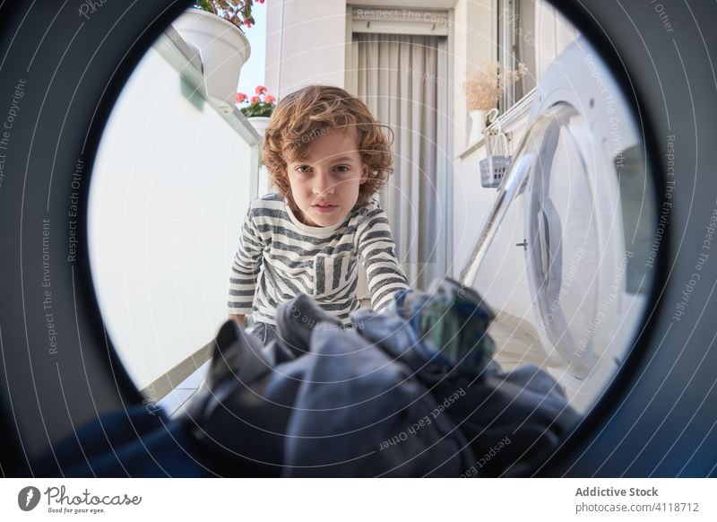 Happy boy taking clothes from washing machine kid laundry home happy take housework household domestic clean smile circle cheerful child routine chore through