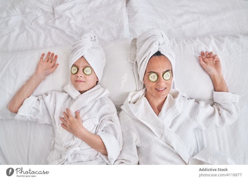 Cheerful woman with kid enjoying spa procedure at home beauty skin care cucumber mask mother together having fun laugh rest cozy positive facial natural smile