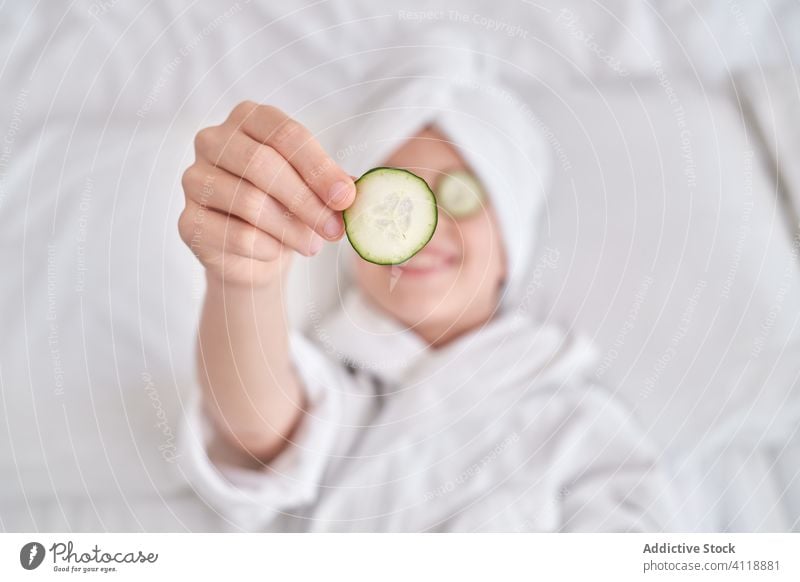 Happy kid enjoying beauty procedure cucumber mask skin care fun positive show slice spa facial joke humor bed playful natural child happy cheerful fresh clean