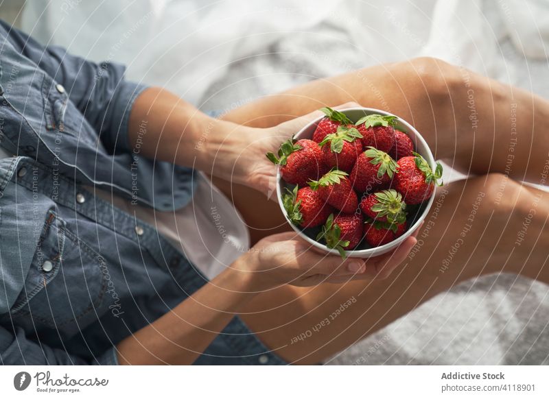 Crop woman with strawberries sitting on bed strawberry bowl home show summer weekend ripe female rest food fruit dessert morning blanket bedroom organic comfort