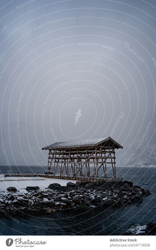 Wooden construction on rocky shore against foggy mountain in winter cloudy day cold fjord ridge snow wooden harbor water overcast lofoten beach norway coast