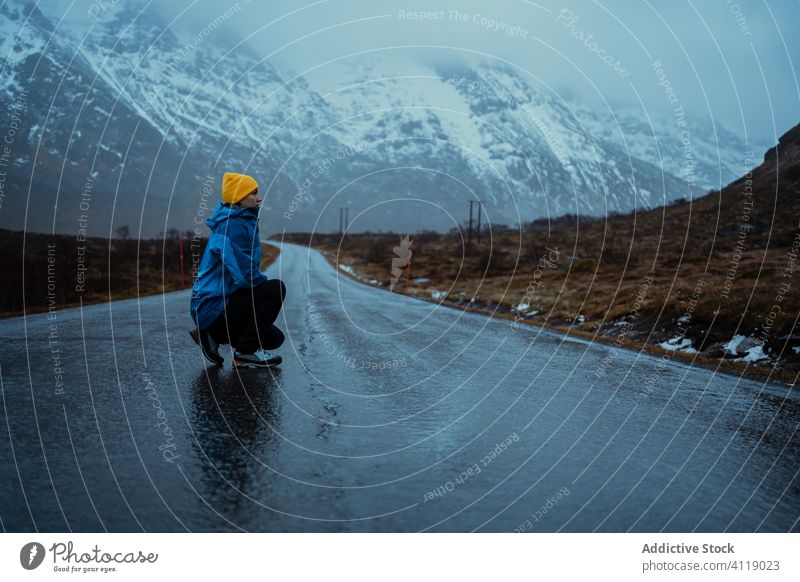 Solitary adult tourist enjoying calm and fresh air on empty road in misty highland in winter woman crouched freedom mountain tourism snow idyllic ridge female