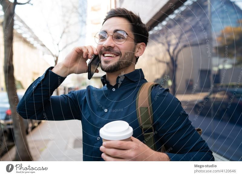 Young man talking on the phone outdoors. young mobile urban coffee take away connection gadget portrait drinking wireless telephone holding walking looking