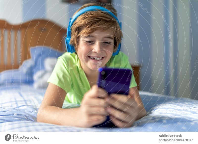 Cheerful kid watching movie on tablet in bedroom gadget home headphones cheerful boy using laugh child online listen internet happy lifestyle device modern