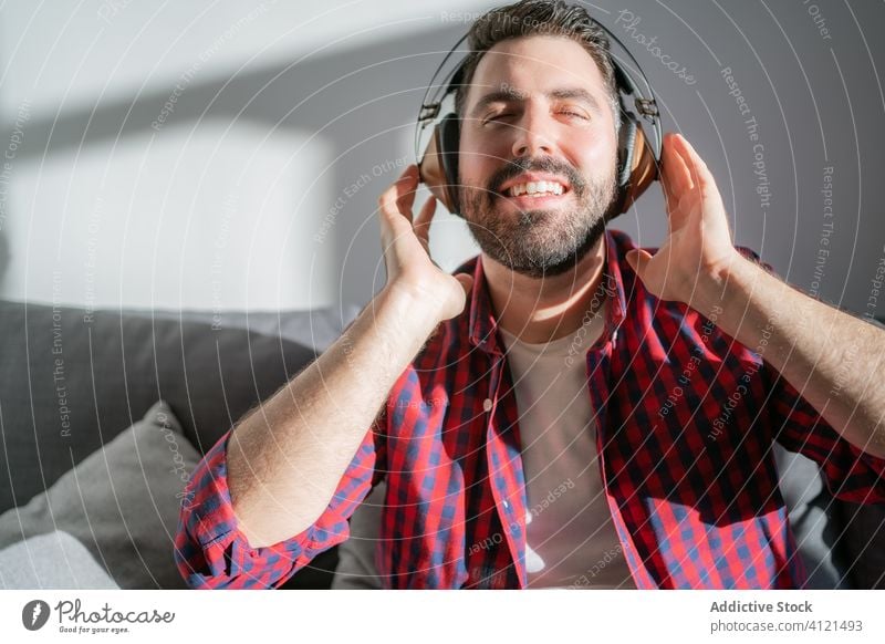 Young man listening to music at home young leisure casual headphones technology caucasian adult lifestyle happy sofa person relaxation modern room indoors