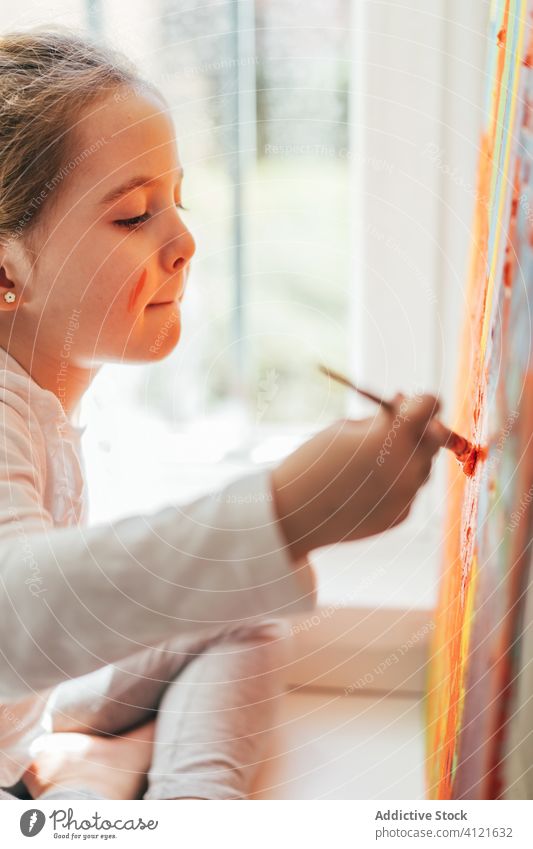 Little girl painting picture with paintbrush canvas draw rainbow creative colorful orange sill casual window art hobby imagination bright sit indoors