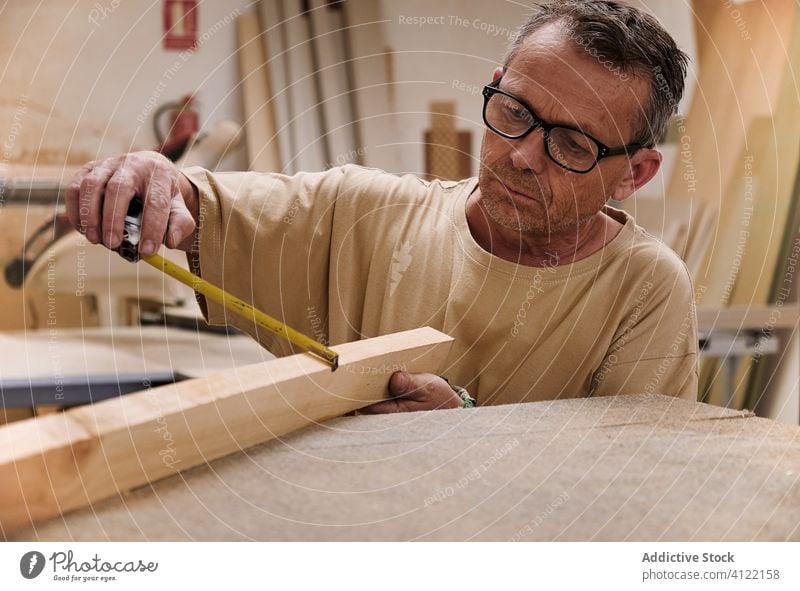 Attentive craftsman using measuring tape while working with lumber in carpentry studio worker control attentive tool precise detail handyman timber wood size