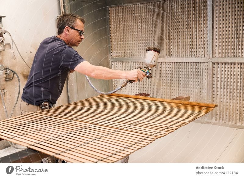 Craftsman applying varnish to wood jalousie using airbrush in carpentry workshop craftsman spray lacquer slats woodwork sprayer tool spray gun wooden airless